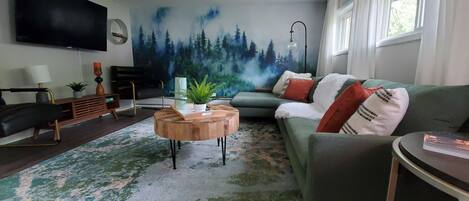 A modern living room with a green sofa, a wooden coffee table, and a large TV mounted on the wall.