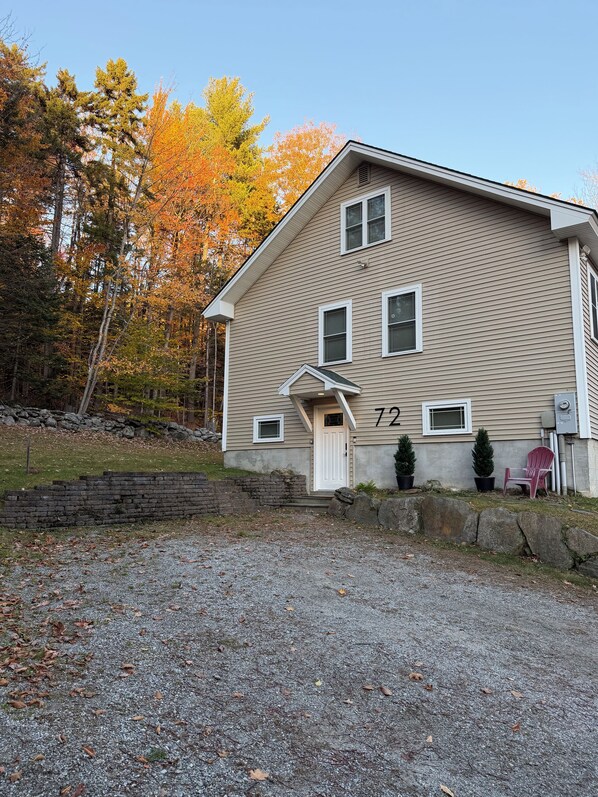 A two-story house with a number '72' on the side, a front porch, and a gravel driveway.