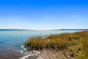 Um lago tranquilo com águas límpidas, um cais que se projeta sobre a água e grama alta ao primeiro plano.