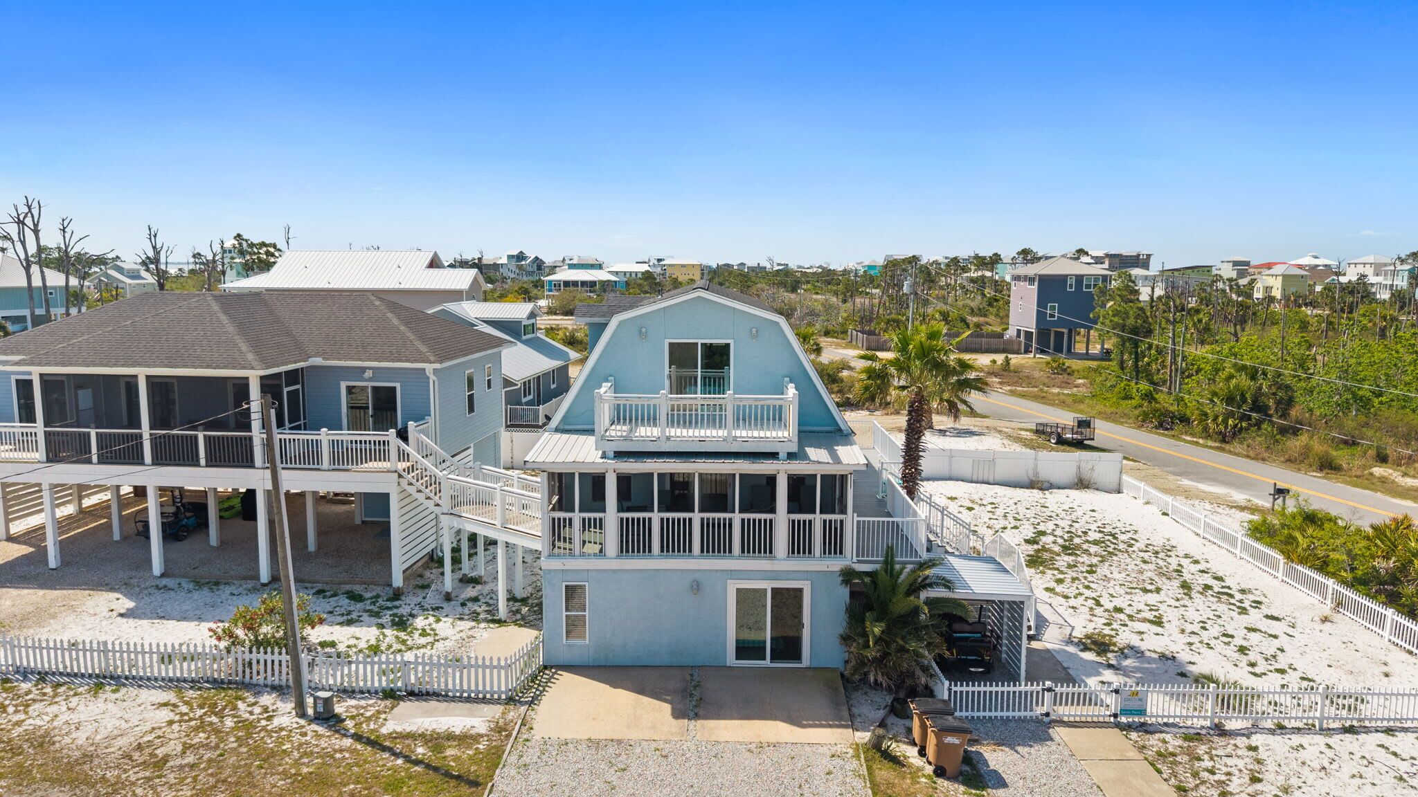 A coastal house with a balcony, a covered porch, and a sandy beach area.