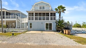 Une maison à deux étages située en bord de mer, dotée d’un balcon, d’une véranda et d’une allée gravillonnée.