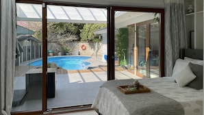 Une chambre dotée d’un grand lit, d’une table de chevet avec un plateau, et offrant une vue sur une piscine à travers des portes vitrées.