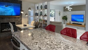 Une cuisine moderne avec des comptoirs en granit, des chaises en cuir rouge et un grand téléviseur à écran plat fixé au mur.