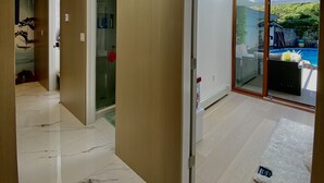 Un intérieur moderne avec un couloir menant à une porte en verre, une piscine visible à travers la porte et un sol en marbre.
