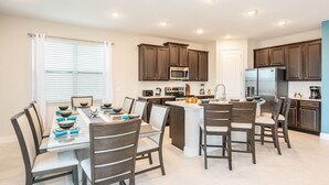 A modern kitchen with dark wood cabinets, stainless steel appliances, and a central island with seating. - Trendy 5BR Villa with Private Pool Near Disney (Kissimmee)