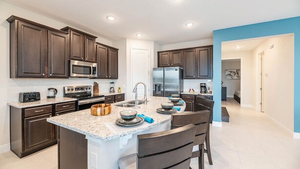 A modern kitchen with dark wood cabinets, stainless steel appliances, and a granite countertop. - Trendy 5BR Villa with Private Pool Near Disney (Kissimmee)