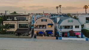 A beachfront property with a two-story house featuring a balcony, a patio with umbrellas, and a view of the ocean. - Steps to the Sand + Patio Lounging | Sunset Water Views | Bay View 3 (San Diego)