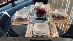 Spisebord dækket med tallerkener, glas og en skål med frugt, omgivet af blå sofaer og et glashoved.
