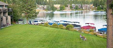 A grassy area with a lake, boats, and a building with a balcony.