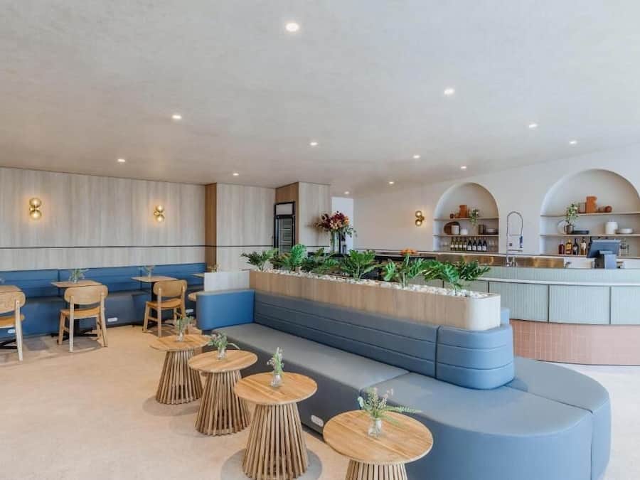 A modern lounge area with wooden tables, blue seating, and a bar counter.