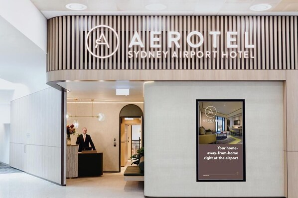 The exterior of the Aerotel Sydney Airport Hotel with a modern design, a reception area, and a sign advertising the hotel's location near the airport. - Aerotel Sydney - Inside International Terminal Airport (Sydney)