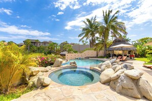 A swimming pool surrounded by rocks and palm trees, with a thatched-roof structure and lounge chairs in the background. - Beautiful Villa in Exclusive Enclave Private Beach. Staff and Concierge included (Cabo San Lucas)