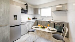 A modern kitchen with a built-in refrigerator, a microwave, and a stove. There is a dining table with two chairs, and a window providing natural light. - Appartement Standing, 90m² Climatisé à 5 mns à Pied de la Croisette et Plages (Cannes)