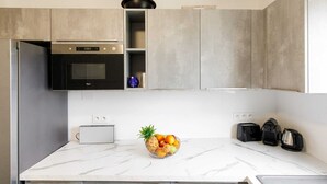A modern kitchen with grey cabinets, a built-in oven, a microwave, and a fruit bowl on the counter. - Appartement Standing, 90m² Climatisé à 5 mns à Pied de la Croisette et Plages (Cannes)