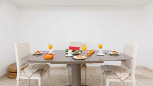 A dining table set with breakfast items including croissants, fruit, and orange juice, surrounded by white upholstered chairs. - Appartement Standing, 90m² Climatisé à 5 mns à Pied de la Croisette et Plages (Cannes)