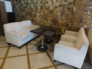 A lobby with a stone mosaic wall, a white sofa, a small table, and a chair. - Triple One Hotel Suites (Abbottabad)