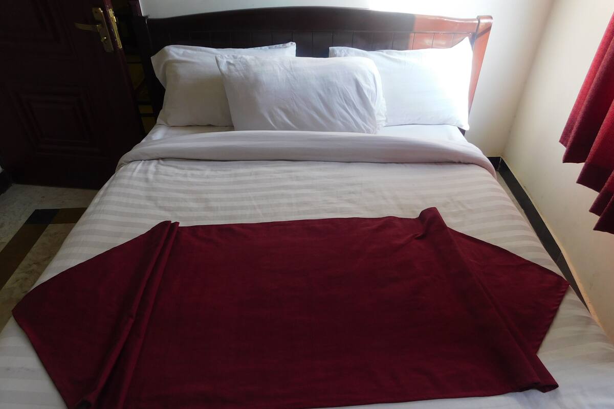 A bed with white linens and a red blanket.