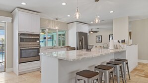 A modern kitchen with white cabinetry, stainless steel appliances, and a central island with bar stools. - Prestigious location, Gulf Access, Heated Pool - Villa Pineapple Oasis - Roelens Vacations (Cape Coral)