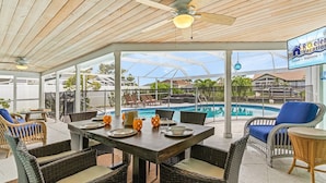 A covered outdoor area with a pool, wicker furniture, and a ceiling fan. - Prestigious location, Gulf Access, Heated Pool - Villa Pineapple Oasis - Roelens Vacations (Cape Coral)
