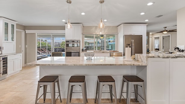 A modern kitchen with a large island, bar stools, pendant lighting, and a view of a pool area. - Prestigious location, Gulf Access, Heated Pool - Villa Pineapple Oasis - Roelens Vacations (Cape Coral)