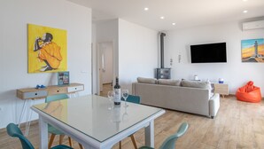 A modern living room with a glass dining table, a sofa, a TV, and artwork on the walls. - Holiday Home "Casa Trafalmar" with Pool, Wi-Fi, Garden and Terrace (Zahora)