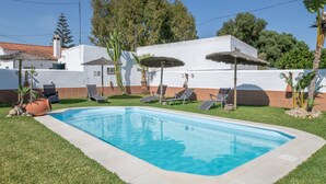 A swimming pool with lounge chairs and umbrellas, surrounded by a white building with a tiled roof. - Holiday Home "Casa Trafalmar" with Pool, Wi-Fi, Garden and Terrace (Zahora)