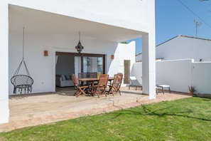 Une terrasse extĂ©rieure avec une table et des chaises, un fauteuil suspendu et une vue sur lâimmeuble voisin.