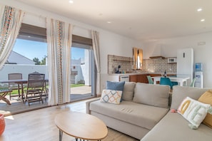 Een woonkamer met een bank, een tafel en uitzicht door een glazen deur op een terras.