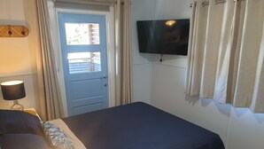 Un dormitorio con cama, televisor montado en la pared, una puerta con ventana y cortinas.