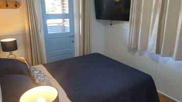 A bedroom with a bed, a TV mounted on the wall, a door with a window, and curtains.