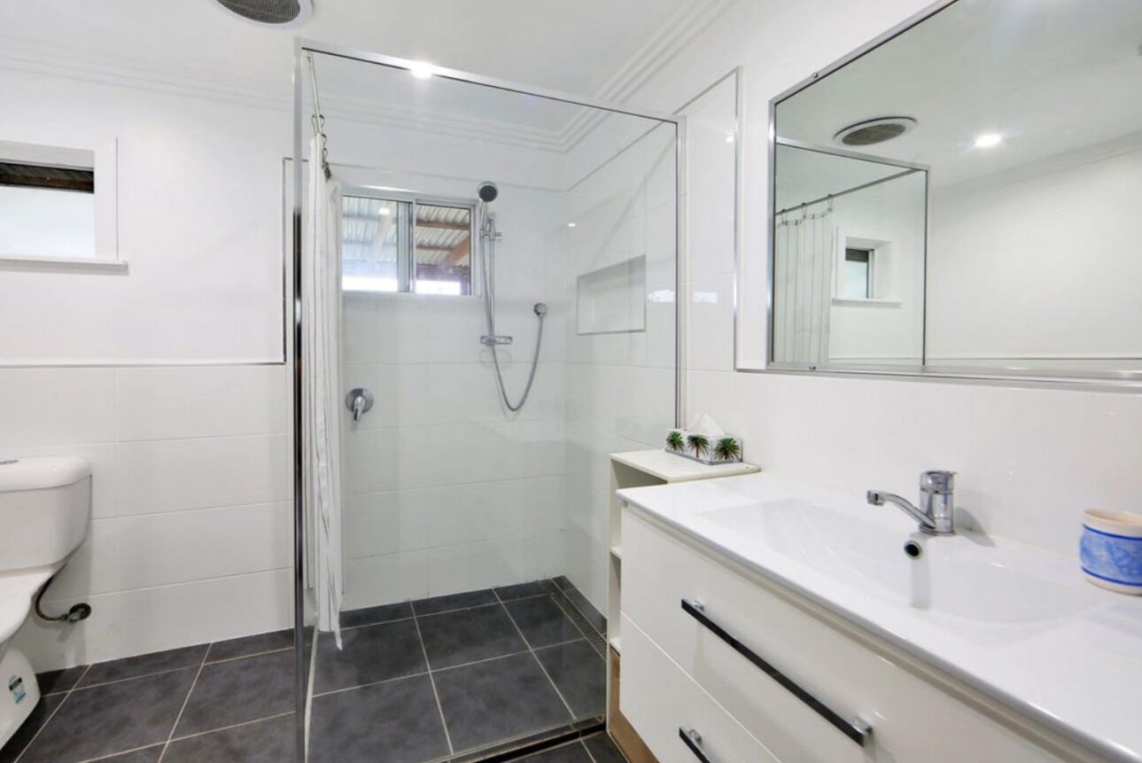 Une salle de bain moderne avec une douche à l’italienne en verre, des carreaux blancs, un grand miroir et un lavabo blanc avec un meuble-vasque.