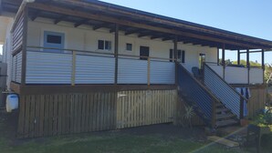 Un edificio de dos pisos con balcón cubierto y terraza de madera.