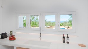 A kitchen with a white countertop, a sink, and three windows with views of trees and a pool. - Villa "Fora" near the Sea with Pool, Wi-Fi, Garden & Terrace (Carovigno)