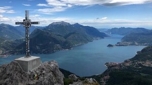 Un monumento en forma de cruz en la cima de una montaña, con vistas a un lago y montañas circundantes.
