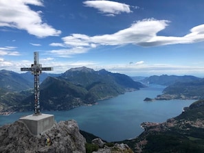 Un monumento a forma di croce in cima a una montagna, con vista su un lago e montagne circostanti.