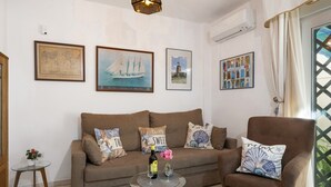 A living room with a sofa, armchair, and a glass coffee table with a bottle and flowers.