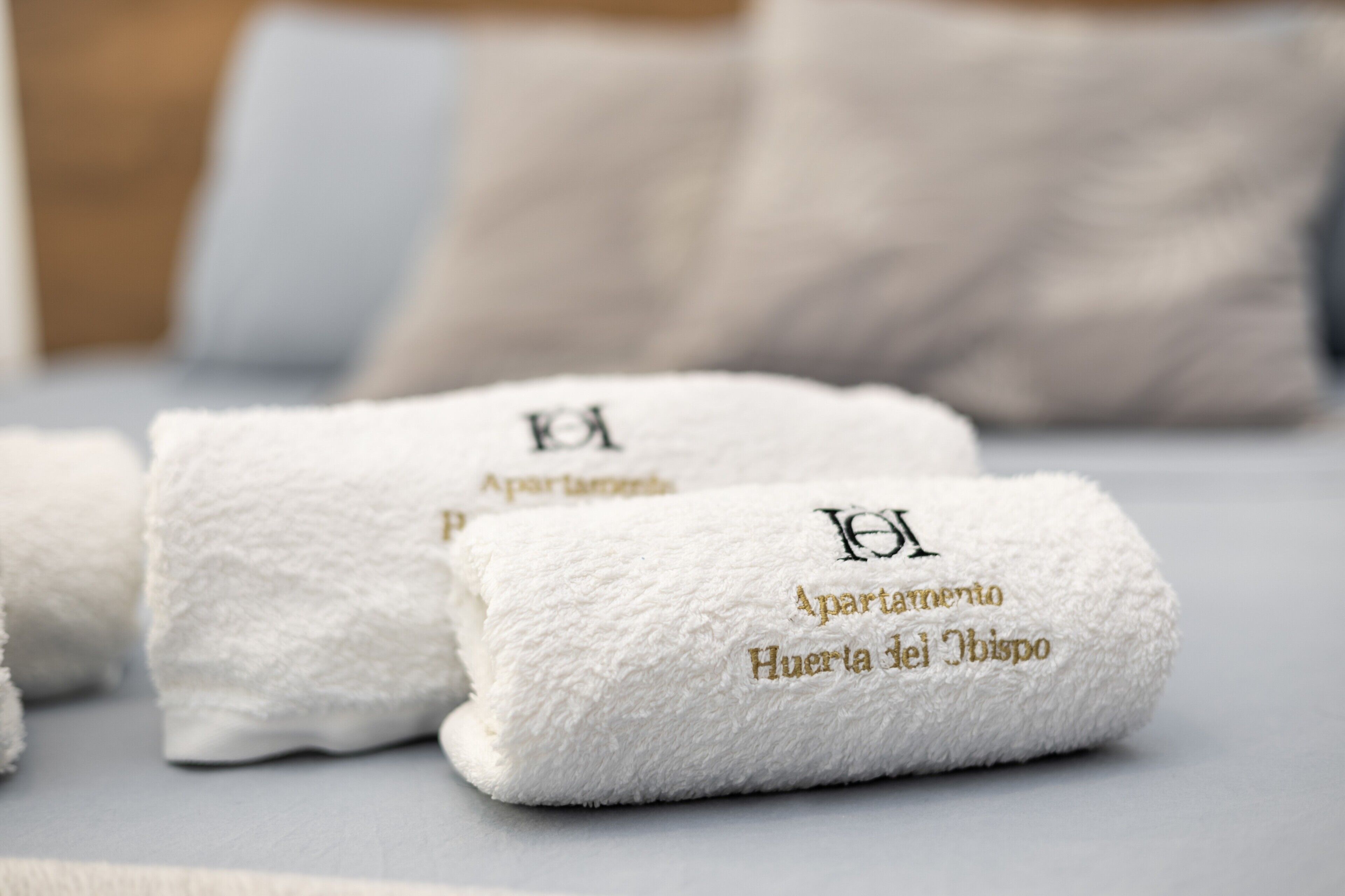 Three white towels with embroidered text on a bed.