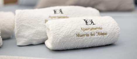 Three white towels with embroidered text on a bed.
