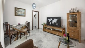 A dining area with a wooden table and chairs, a television, and a cabinet with glassware.