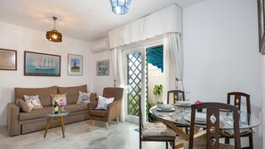 A living room with a sofa, armchair, glass coffee table, and a dining table with chairs.