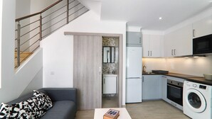 Un espace de vie compact comprenant un canapé, une table basse, un lave-linge, un coin cuisine et un escalier.