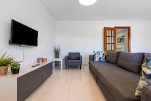 A modern living room with a flat-screen TV, a sofa, a chair, a small table, and a cabinet.