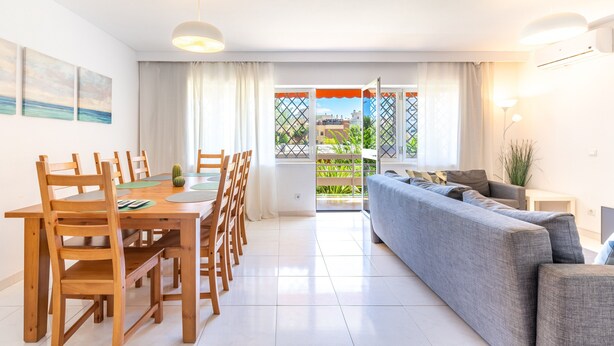 A modern living room with a grey sofa, wooden dining table with chairs, and a view through a glass door to an outdoor area. - Apartment 'Eurosol Carihuela' with Shared Garden, Wi-Fi and Air Conditioning (Torremolinos)