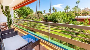 A balcony with wicker furniture, a pool, and a view of palm trees and greenery. - Apartment 'Eurosol Carihuela' with Shared Garden, Wi-Fi and Air Conditioning (Torremolinos)