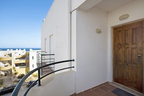 A balcony with a metal railing, a wooden door, and a view of other buildings and the sea.