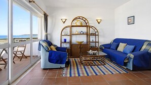 A balcony with a view, a blue sofa, a chair, a small table, and a decorative shelf.
