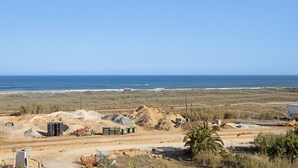 A construction site with piles of sand and gravel, a road, and a clear view of the ocean.