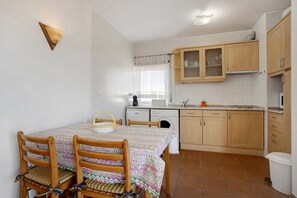 A kitchen with wooden cabinets, a dining table with chairs, and a window with curtains.