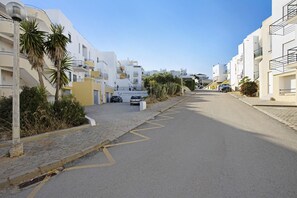 A residential street with modern white buildings, a paved road with yellow markings, and a parked car.