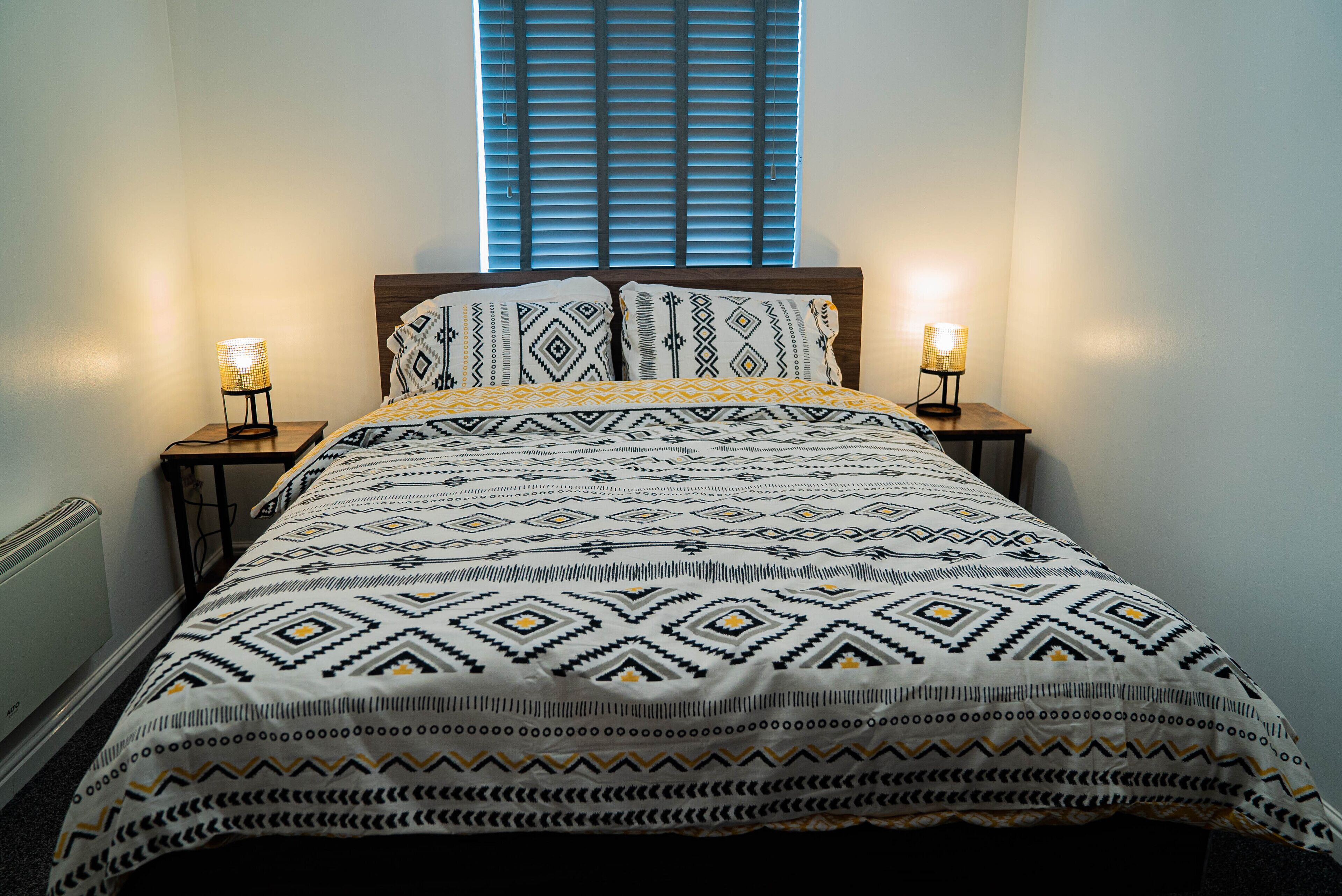 A bed with a patterned bedspread and two bedside lamps.